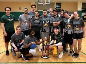 College students in athletic gear pose around a trophy.