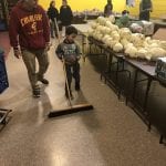 A child pushing a broom marvels at a table full of produce.