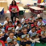 Young children sit on a school floor, holding copies of the book Police In Our School.