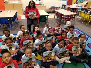 Young children sit on a school floor, holding copies of the book Police In Our School.