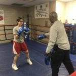 A young woman spars with an adult in a boxing ring.