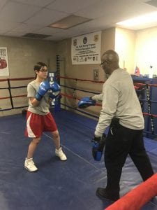 A young woman spars with an adult in a boxing ring.