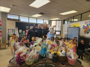 Officers and the Easter Bunny pose with a classroom full of smiling students and donated Easter baskets.