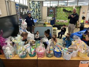 Students gather around a seated Easter Bunny and community officers in a colorful classroom setting.