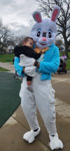 Person in an Easter Bunny costume gently holds a small child at the park.