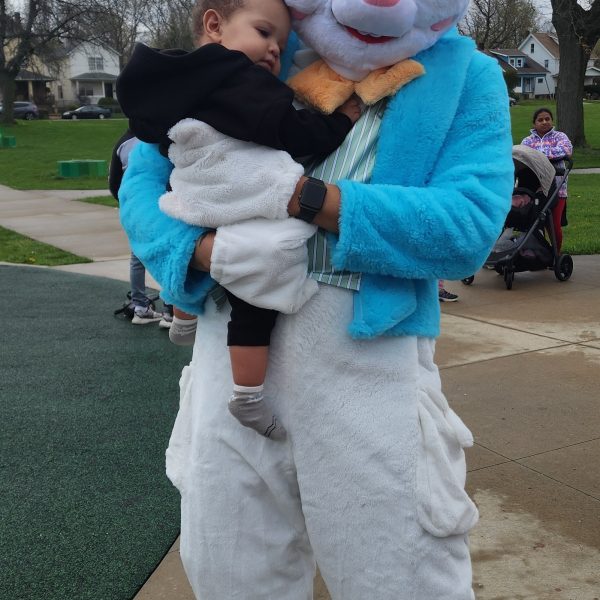 Person in an Easter Bunny costume gently holds a small child at the park.
