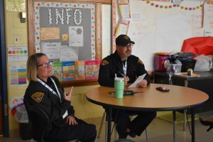 Two First District officers seated at a classroom roundtable, reviewing interview materials and listening to a student presentation.
