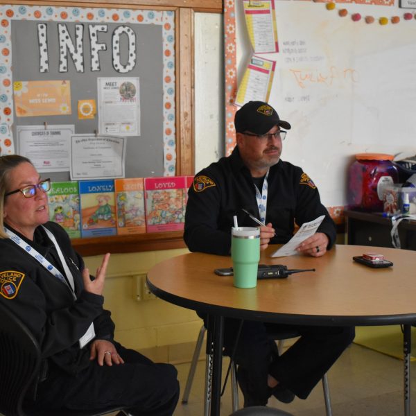Two First District officers seated at a classroom roundtable, reviewing interview materials and listening to a student presentation.
