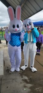Two people in Easter Bunny costumes pose under a pavilion, making playful gestures toward the camera.