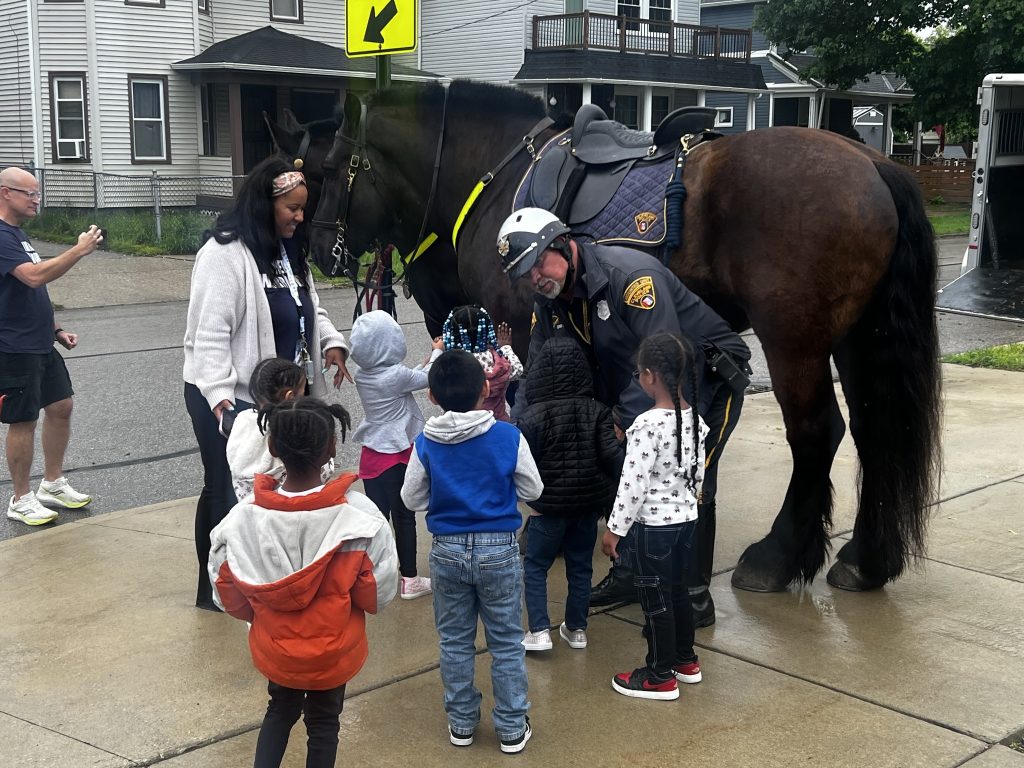 Mounted Unit officer introduces children to one of the patrol horses while students and staff gather around.