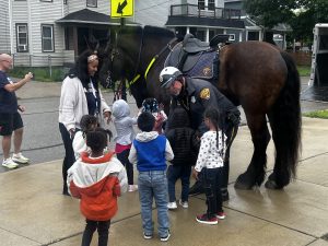 Mounted Unit officer introduces children to one of the patrol horses while students and staff gather around.