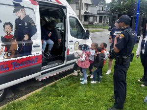 Kids talk with officers near the community outreach van decorated with cartoon-style police art.
