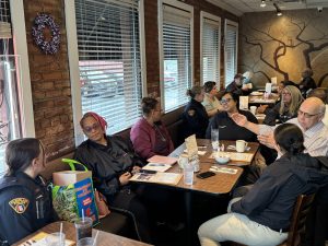 Group photo of officers and residents seated at a long table during Coffee with a Cop