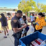 Officer distributing toys and speaking with students near vendor booths