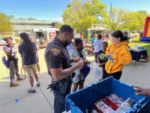 Officer distributing toys and speaking with students near vendor booths