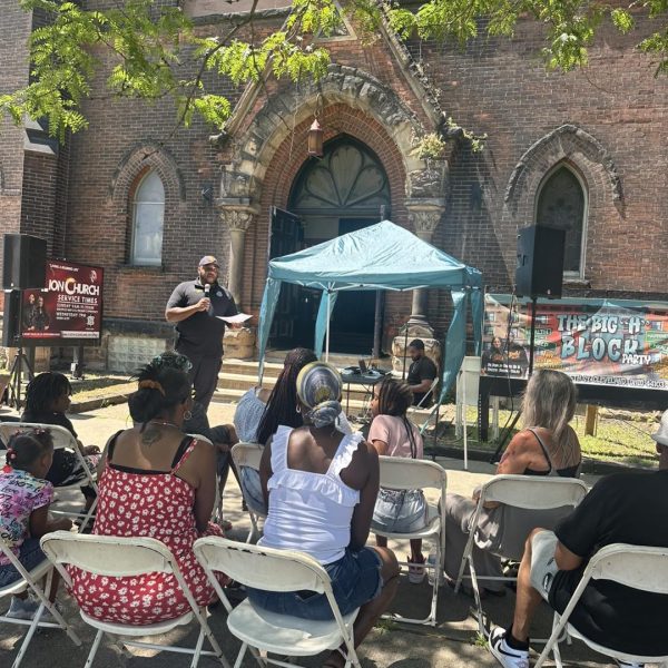 Community members seated during a daytime gathering outside The Lion Church as a speaker presents