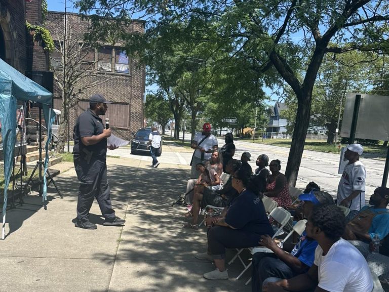 Speaker addresses seated guests under a tent in front of The Lion Church during the block party