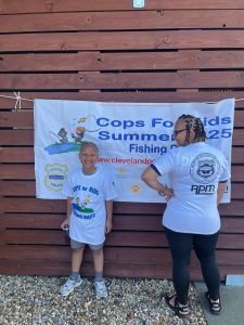 A young participant and an adult stand in front of the Cops for Kids Summer 2025 Fishing Days banner.