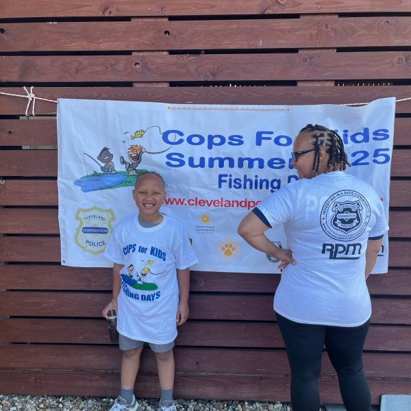 A young participant and an adult stand in front of the Cops for Kids Summer 2025 Fishing Days banner.
