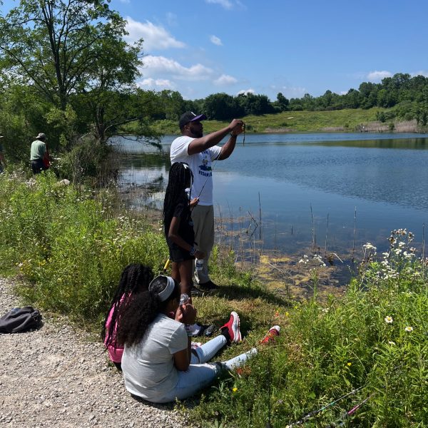 Children and adults fish along the lakeshore on a bright summer day at the Cops for Kids event.
