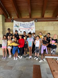 A group of kids and volunteers pose with a banner and prizes at the conclusion of the fishing event.
