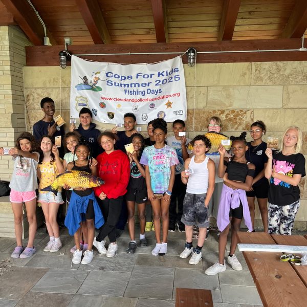 A group of kids and volunteers pose with a banner and prizes at the conclusion of the fishing event.
