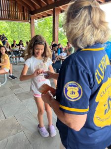 An officer from Cleveland PAL hands a prize card to a smiling young girl under the event pavilion.