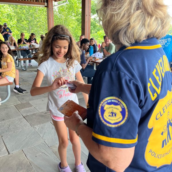 An officer from Cleveland PAL hands a prize card to a smiling young girl under the event pavilion.