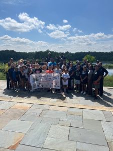 A large group of officers, kids, and community members pose together with the event banner near the water.