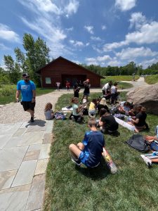 Children and volunteers gather on the grass with their fishing rods and prizes under a sunny sky.