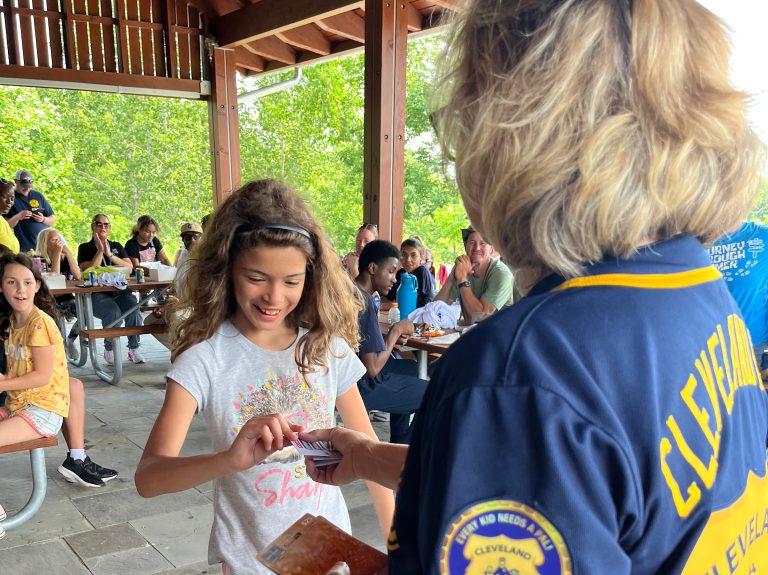 An officer from Cleveland PAL hands a prize card to a smiling young girl under the event pavilion.