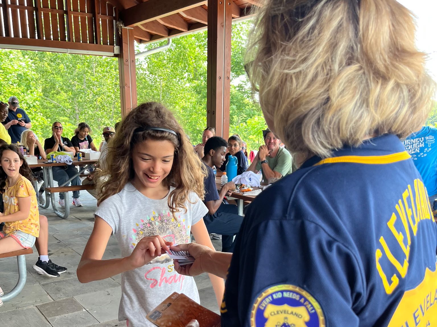 An officer from Cleveland PAL hands a prize card to a smiling young girl under the event pavilion.