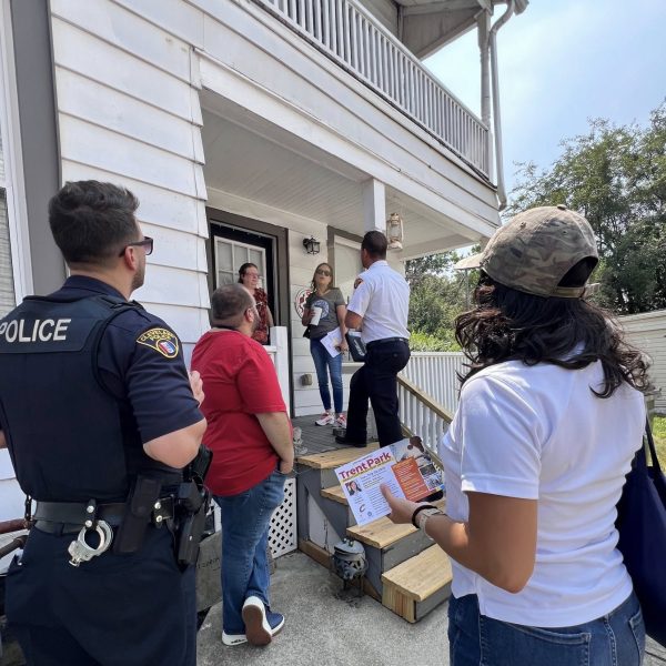 Officers and community partners visit a resident on her porch during the safety walk, with one woman holding a Trent Park flyer.