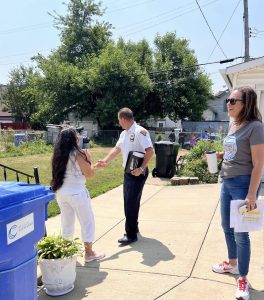 Commander Maffo-Judd shakes hands with a resident outside her home while Councilwoman Santana observes with a smile and coffee in hand.