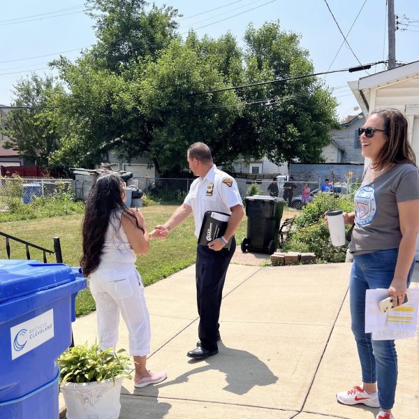 Commander Maffo-Judd shakes hands with a resident outside her home while Councilwoman Santana observes with a smile and coffee in hand.