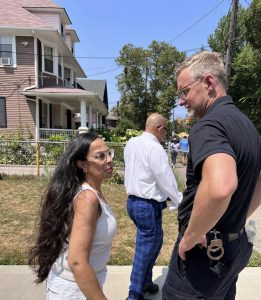 Sergeant Thomas and a community member chat casually on the sidewalk, with other participants visible in the background.