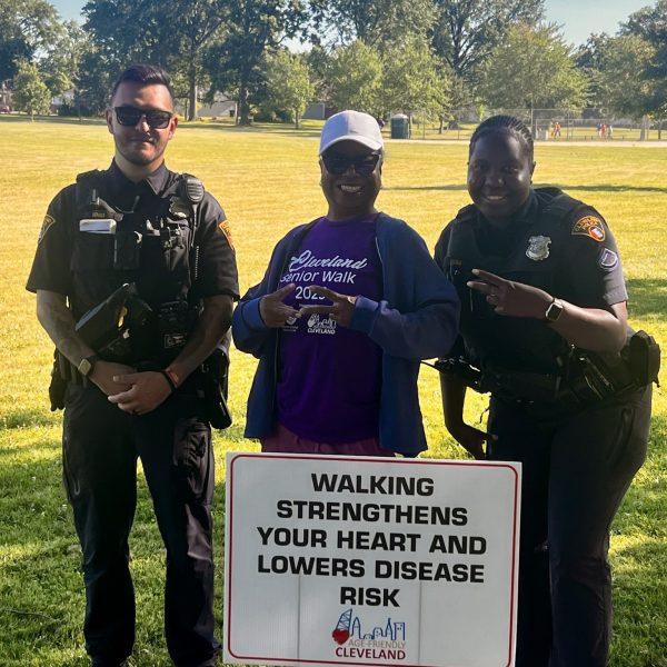 Two officers stand with a smiling senior participant in front of a Cleveland Senior Walk sign promoting heart health.