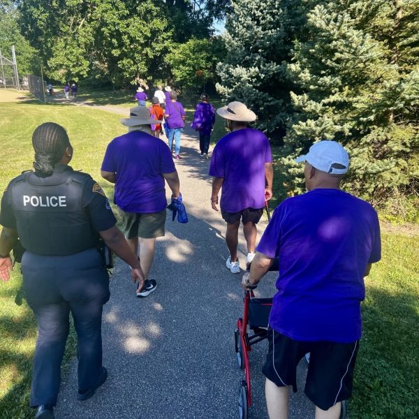 Officer walks alongside senior participants wearing matching purple shirts on the paved path at Loew Park.