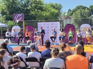Event speakers sit on stage near the newly renovated basketball court as a community audience watches.