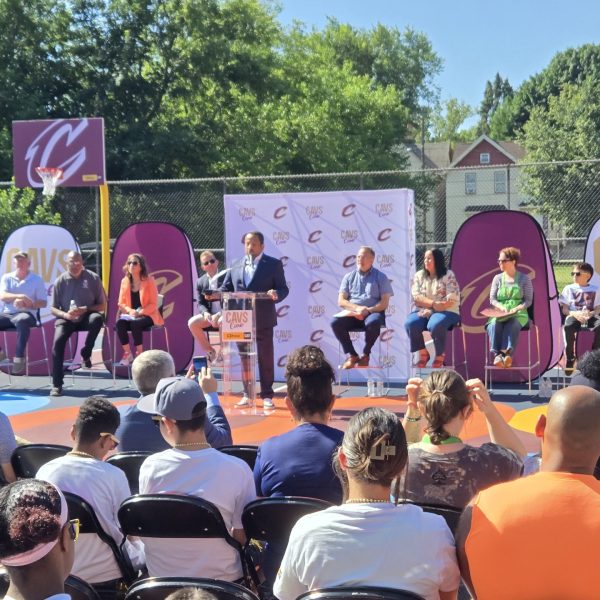 Event speakers sit on stage near the newly renovated basketball court as a community audience watches.