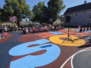 Rows of chairs set up on the newly painted Trent Park basketball court with a crowd gathering in the background for the event.