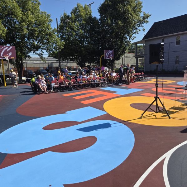 Rows of chairs set up on the newly painted Trent Park basketball court with a crowd gathering in the background for the event.
