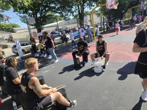 Members of a Cavs drumline perform on plastic buckets while cheerleaders and event attendees gather along the court perimeter.