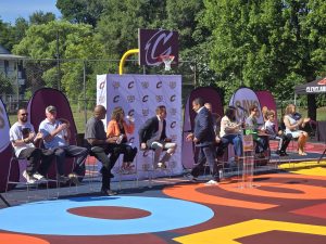 Cavs Care panelists seated onstage, applauding as a speaker prepares to take the podium during the Trent Park court dedication ceremony.