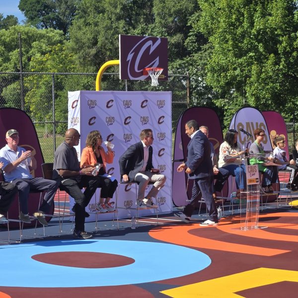 Cavs Care panelists seated onstage, applauding as a speaker prepares to take the podium during the Trent Park court dedication ceremony.