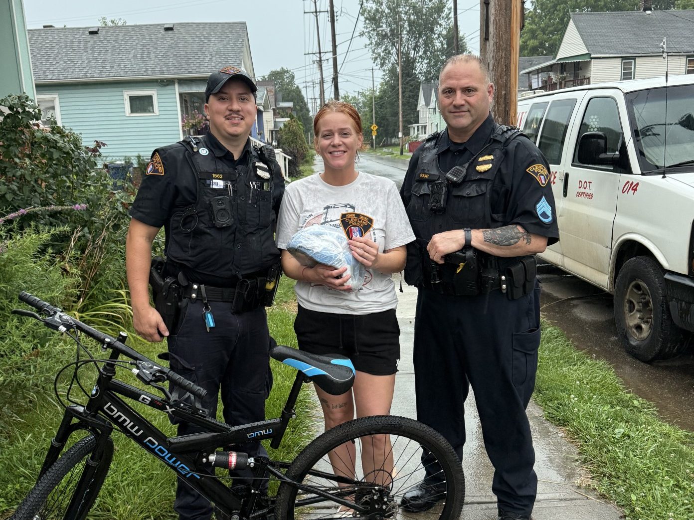 Patrol Officer Luis Melendez and Sgt. Tom Ross stand with the mother of the young rider who received a donated bicycle and helmet, posing together beside the new bike.