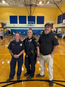 Three First District officers smile for a photo in the RG Jones School gym during Family Night.