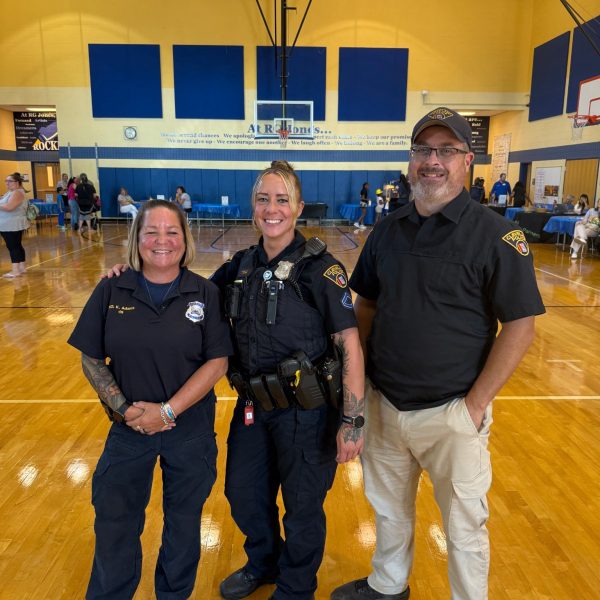 Three First District officers smile for a photo in the RG Jones School gym during Family Night.