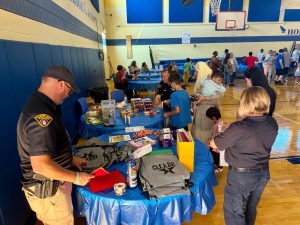 Officers and volunteers distribute supplies from tables covered in school items as families line up during RG Jones School’s Family Night.