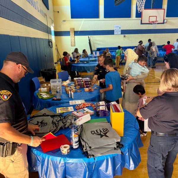 Officers and volunteers distribute supplies from tables covered in school items as families line up during RG Jones School’s Family Night.